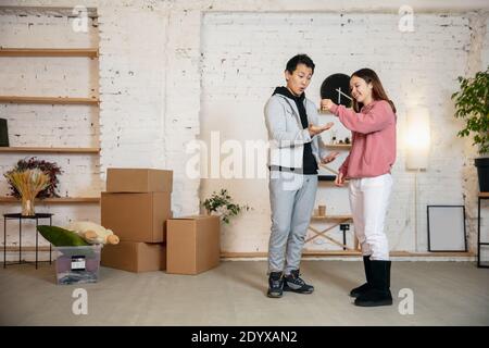 Obtention des clés. Nouveaux propriétaires, jeune couple déménagement à la nouvelle maison, appartement, look heureux. Rêve, amour, relation, immobilier et concept intérieur. Nouvelle vie ensemble. Femme caucasienne et homme asiatique. Banque D'Images