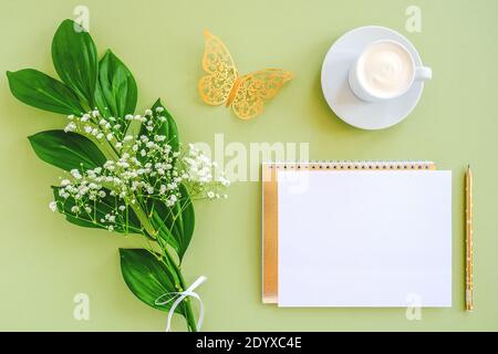 Espace de travail avec bloc-notes vierge, crayon, feuille verte, papillon doré décoratif et tasse à café sur fond vert. Maquette vue de dessus Flat lay T Banque D'Images