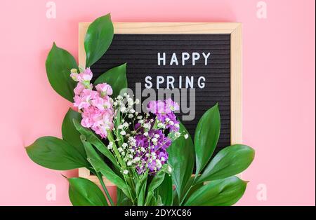 Texte « Happy Spring » sur tableau noir et bouquet de fleurs sur fond rose. Concept Bonjour printemps, printemps. Modèle pour carte postale, message d'accueil c Banque D'Images