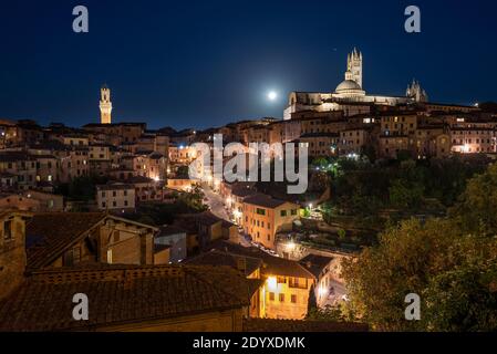 Pleine lune sur une allée illuminée et le panorama de la vieille ville médiévale de Sienne avec la cathédrale, tour de l'horloge de la mairie, Toscane, Italie Banque D'Images