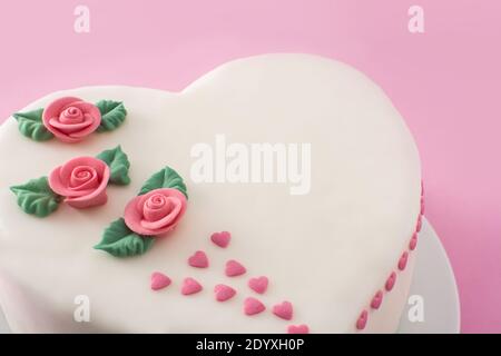 Gâteau de coeur pour la Saint-Valentin, la fête des mères ou l'anniversaire, décoré de roses et de coeurs de sucre roses sur fond rose Banque D'Images