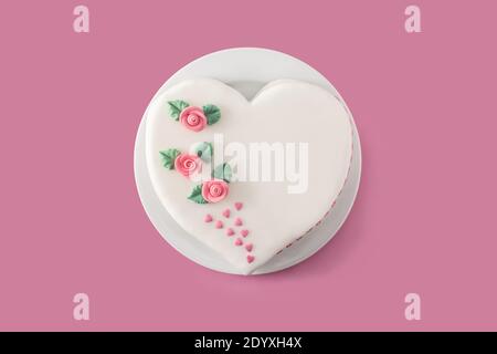 Gâteau de coeur pour la Saint-Valentin, la fête des mères ou l'anniversaire, décoré de roses et de coeurs de sucre roses sur fond rose Banque D'Images