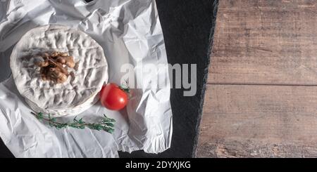 Fromage aux noix et à la tomate. Délicieux fromage brie sur fond noir. Type Brie de fromage. Camembert. Du Brie frais et une tranche sur un plateau en pierre. Banque D'Images