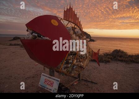 Sur la plage, une grande poubelle en forme de poisson est pleine de déchets Banque D'Images