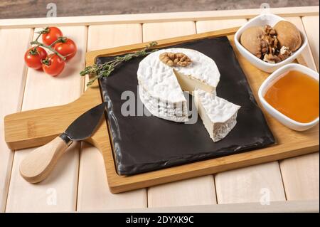 plateau en bois pour le petit déjeuner avec du brie, du miel, des noix, de la tomate. petit déjeuner au fromage sur le plateau en bois avec une assiette noire Banque D'Images