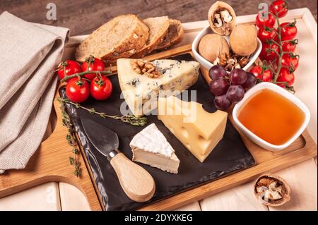 plateau en bois pour le petit déjeuner avec assortiment de fromages différents, miel, noix, tomate. dessert au fromage sur le plateau en bois avec assiette noire. image en tons Banque D'Images