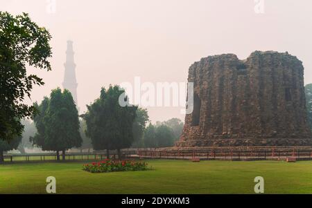 À l'intérieur du complexe Qutb Minar avec ses ruines anciennes et vue sur le grand minaret englouti par le smog et la brume entouré de jardins à Delhi, en Inde. Banque D'Images