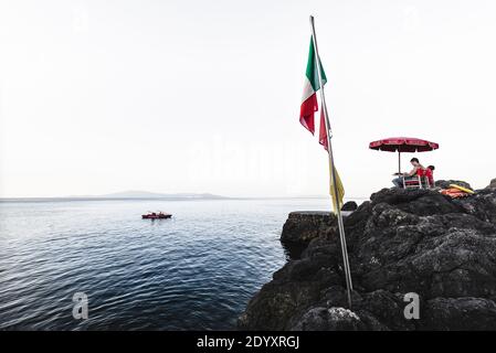 Les sauveteurs du Bagno delle donne sont assis sur des chaises sur les rochers de Talamone en début de matinée, contre une vue sur la mer et Monte Argentario, Italie Banque D'Images