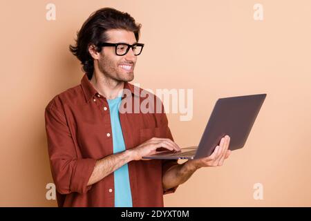 Portrait photo d'un homme tenant un ordinateur portable en dactylographie à la main isolée sur fond beige pastel Banque D'Images