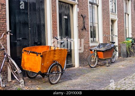 Deux vélos de transport hollandais modernes en face des maisons médiévales. Les vélos sont aujourd'hui utilisés par les parents urbains pour faire du vélo à leurs enfants jusqu'à l'école. Banque D'Images