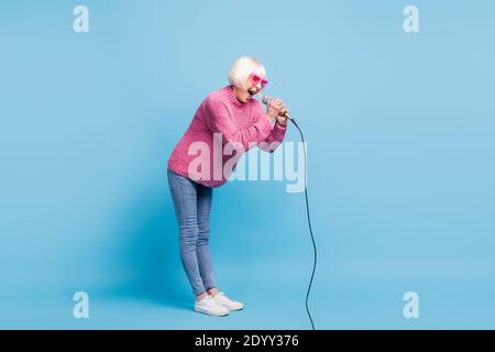 Portrait plein écran d'une vieille dame hurlant tenant un microphone en deux mains isolées sur fond bleu pastel Banque D'Images