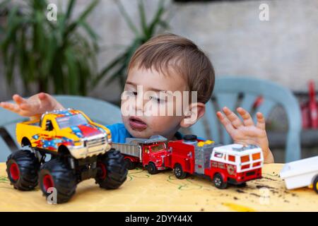 Un enfant joue avec ses nouveaux jouets, un camion de pompiers, un camion de monstres et un camion. Banque D'Images