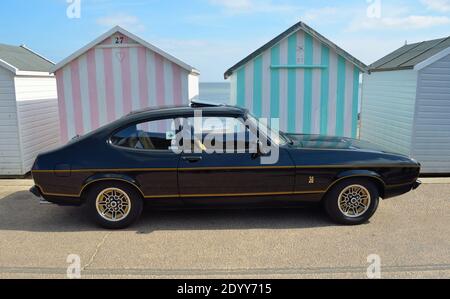 Classic Black Ford Capri 3.0 litres voiture garée sur la promenade du front de mer en face de cabines de plage. Banque D'Images