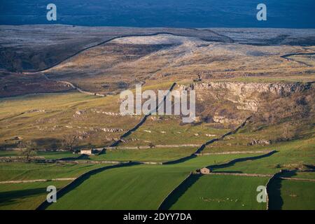 La lumière du soleil d'hiver ramasse les murs en pierre sèche et les vieilles granges près de Langcliffe dans les Yorkshire Dales, avec l'imposante cicatrice de Reinsber se levant derrière. Banque D'Images