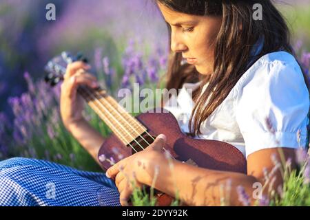 Portrait d'une belle fille de pays qui joue sur le ukulele parmi les fleurs de lavande Banque D'Images