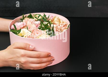 Boîte cadeau rose avec composition florale dans les mains des femmes sur le fond noir avec espace de copie. Cadeau pour la Saint-Valentin, International Women's Banque D'Images