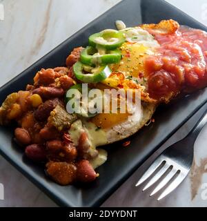 Deux œufs mexicains frits avec piment salsa et jalapeno en tranches servi huevos style rancheros Banque D'Images