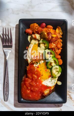 Deux œufs mexicains frits avec piment salsa et jalapeno en tranches servi huevos style rancheros Banque D'Images