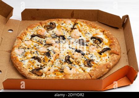 Fermer la pizza avec les champignons et les crevettes dans une boîte en carton ouverte sur une table en bois blanc. Mise au point peu profonde. Banque D'Images