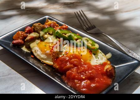 Deux œufs mexicains frits avec piment salsa et jalapeno en tranches servi huevos style rancheros Banque D'Images