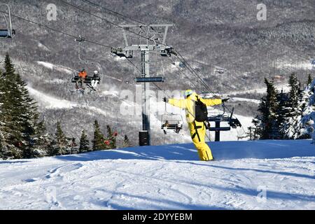 Snowboardeur en descente sur les pistes, vêtu d'une monocombinaison jaune par temps ensoleillé avec de la neige fraîche. Station de ski de Stowe Mountain, VT 2020. Image haute résolution Banque D'Images