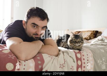 Beau jeune homme sur un lit avec joli chat tabby Banque D'Images