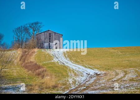Grange de tabac assise sur une colline avec un sentier couvert de neige. Banque D'Images