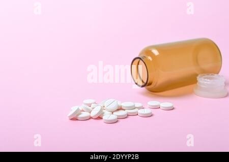 Pilules blanches rondes dispersées d'une bouteille brune sur fond rose. Thème pharmacie et soins de santé. Antécédents médicaux. Copier l'espace. Banque D'Images