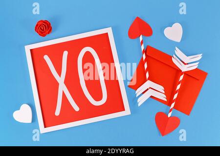 Composition de la Saint-Valentin avec cadre avec texte « XO », flèches d'amour de cupidon, lettre et coeurs sur fond bleu Banque D'Images