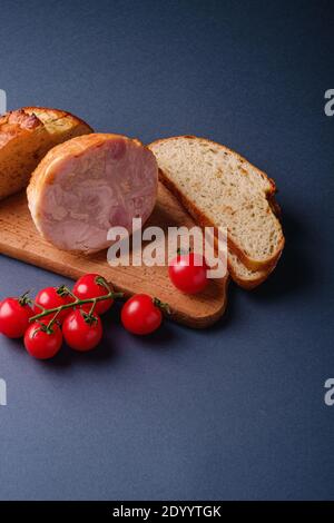 Viande de jambon de dinde, branche de tomates cerises fraîches et pain coupé en tranches sur planche à découper en bois, fond bleu minimal, vue d'angle, espace de copie Banque D'Images