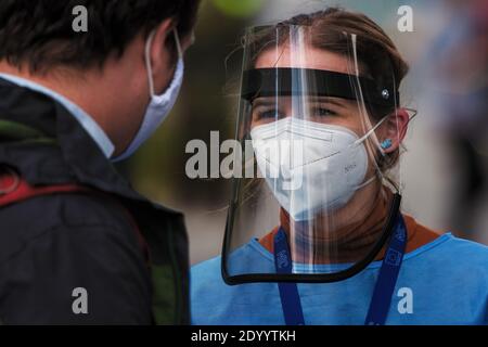 Jeune médic portant un respirateur et un masque facial en plastique parlant à un homme en attente d'un test du virus corona. Banque D'Images