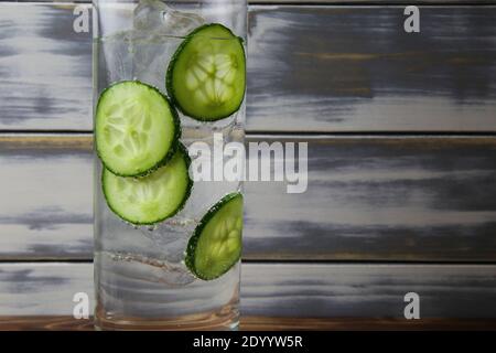 Gros plan de verre à cocktail isolé avec des tranches de concombre tonique de gin et des cubes de glace. planches anciennes en bois avec arrière-plan de l'espace de copie. Banque D'Images