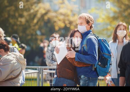 Embrassant le couple amoureux avec des masques faits maison en tissu qui attendent en ligne de personnes pour le test d'immunité collective contre le virus corona. Banque D'Images