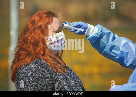 Femme avec masque facial en tissu étant mesurée par un thermomètre numérique tenu dans la main du médic. Banque D'Images
