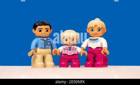 Emballage de trois figurines Lego représentant une famille modèle heureuse (papa, maman et fille souriant) isolée sur fond bleu. Banque D'Images