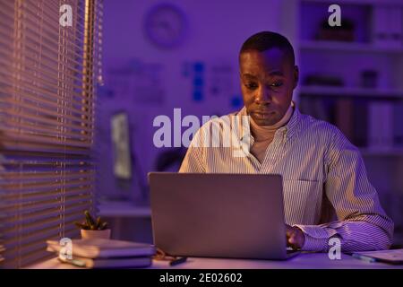 Jeune adulte fatigué Africain américain homme travaillant tard dans la soirée sur un projet important utilisant un ordinateur portable, espace de copie Banque D'Images