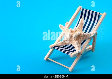 Détente sur les vacances et les activités d'été concept avec une étoile de mer sur une chaise longue ou une chaise longue isolée sur bleu minimaliste arrière-plan avec espace de copie Banque D'Images