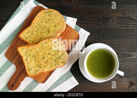 Paire de toasts au beurre d'ail sur le bareboard avec une tasse De thé vert chaud sur une table en bois Banque D'Images