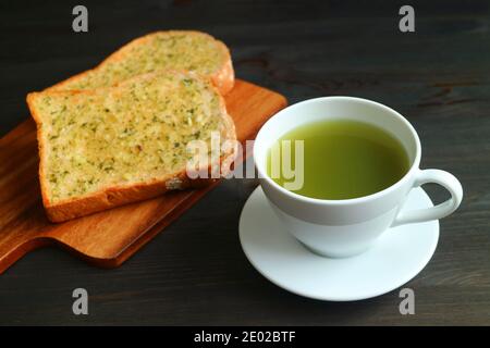 Fermer une tasse de thé vert chaud avec de l'ail flou Toasts au beurre sur une table en bois noir Banque D'Images