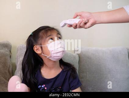 Une mère surveille périodiquement la température de sa fille à l'aide d'un thermomètre infrarouge sur son front, concernant une épidémie de virus Corona. Banque D'Images