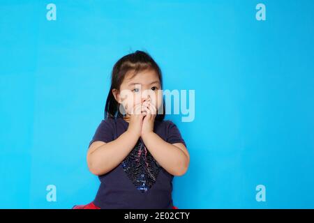 Une jolie fille asiatique couvrant sa bouche avec ses mains avec surprise. Fond bleu clair Uni. Banque D'Images