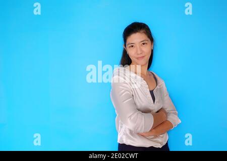 Un corps de taille représentant une femme asiatique d'affaires attrayante et confiante, les bras croisés, souriant sur un fond bleu clair et Uni. Banque D'Images