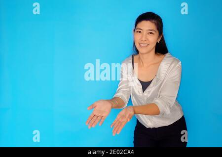 Une prise de vue à la taille d'une femme asiatique attirante dans ses années 30 présentant un produit, pointant avec des mains ouvertes sur un fond bleu clair Uni. Banque D'Images