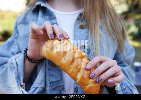 une fille mange un petit pain avec du chocolat dans la rue. Restauration rapide Banque D'Images