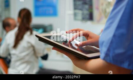 Gros plan de l'infirmière tenant et tapant sur un comprimé debout dans une clinique stomatologique, tandis que le médecin travaille avec le patient en arrière-plan. Utilisation du moniteur avec la touche chroma izolated pc key maquette pc display Banque D'Images