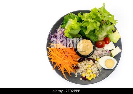 Salade végétale saine de tomates fraîches, carottes, chêne vert, maïs, millet, œuf, chou pourpre et vinaigrette sur assiette noire. Menu régime. Végétalien Banque D'Images