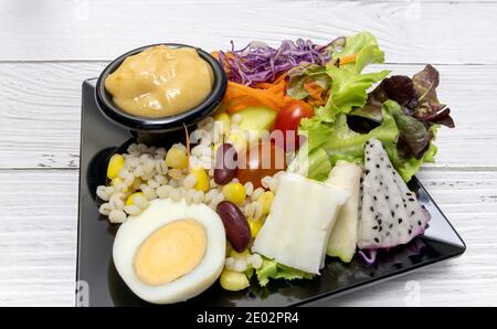 Salade végétale saine de tomates fraîches, carottes, chêne vert, maïs, millet, œuf, chou pourpre et vinaigrette sur assiette noire. Menu régime. Foo végétalien Banque D'Images