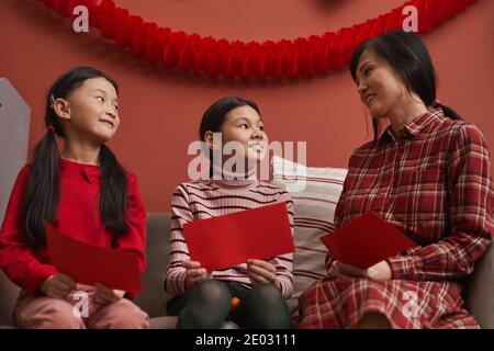 Femme chinoise moderne qui passe du temps chez elle avec son petit enfant Filles préparant des enveloppes rouges pour les cadeaux du nouvel an lunaire Banque D'Images