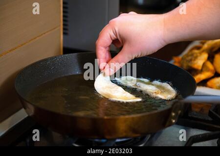 Gros plan de la main mettant des boulettes de gyoza avec remplissage de champignons dans une poêle chaude. Boulettes croquantes dorées cuisant dans l'huile. Banque D'Images