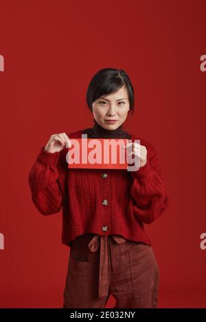 Portrait moyen long en studio réalisé par une femme asiatique à la mode enveloppe rouge sur fond rouge Banque D'Images